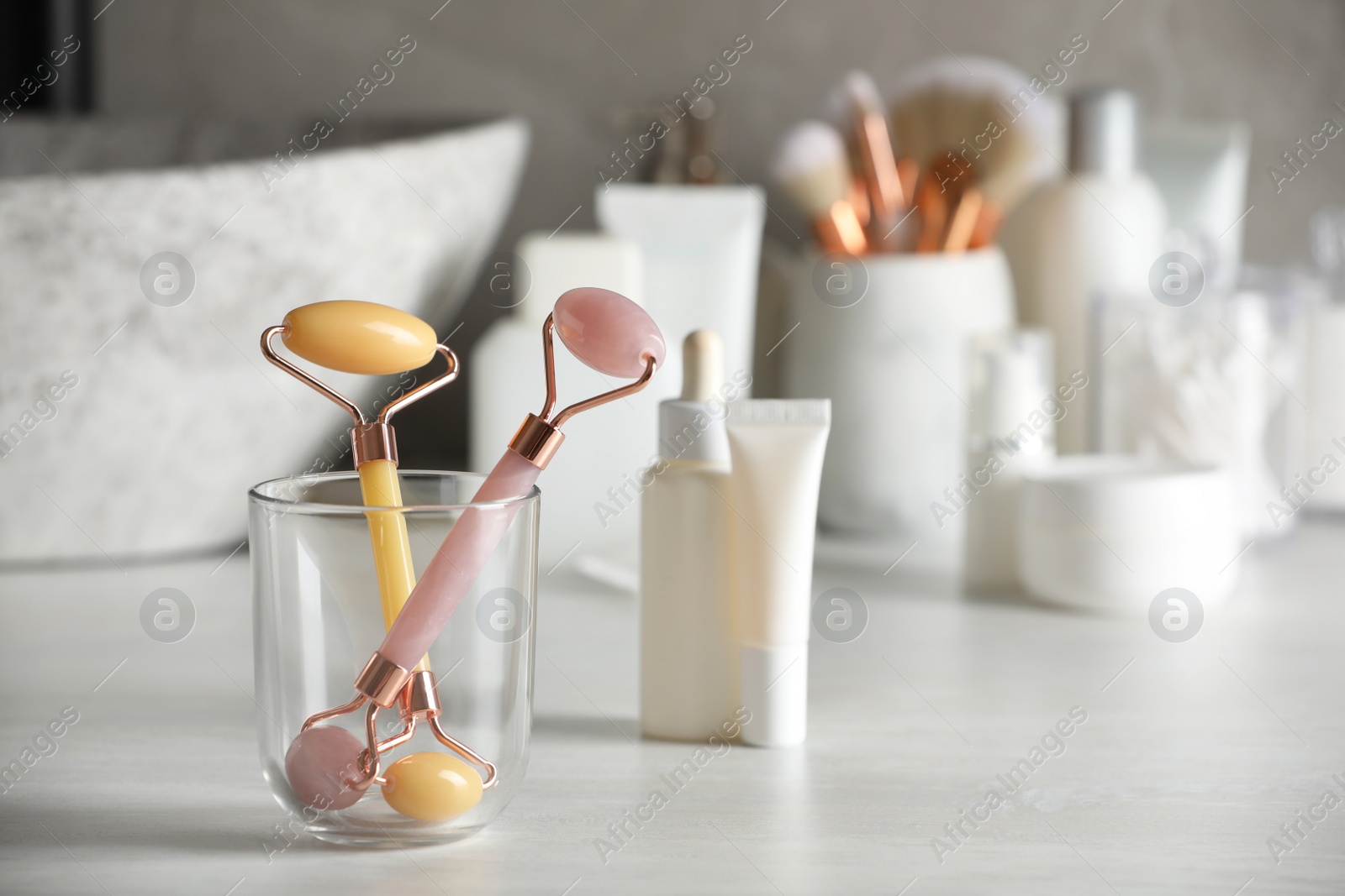 Photo of Natural face rollers and cosmetic products on counter in bathroom. Space for text