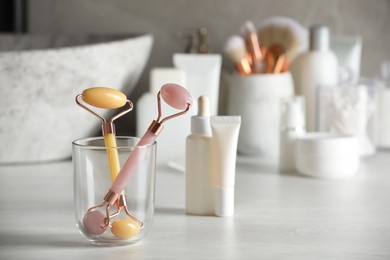 Photo of Natural face rollers and cosmetic products on counter in bathroom. Space for text