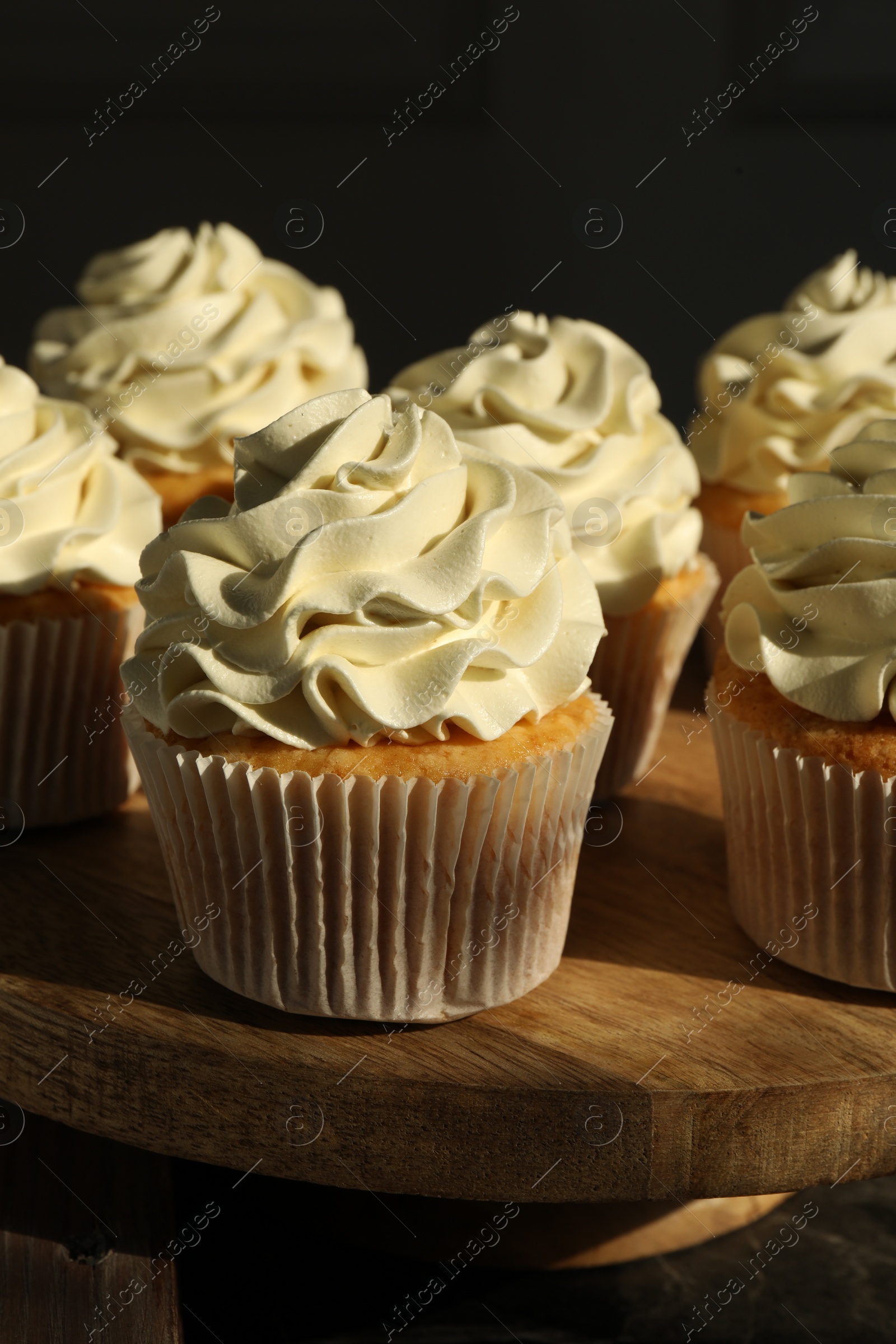 Photo of Tasty cupcakes with vanilla cream on wooden stand, closeup