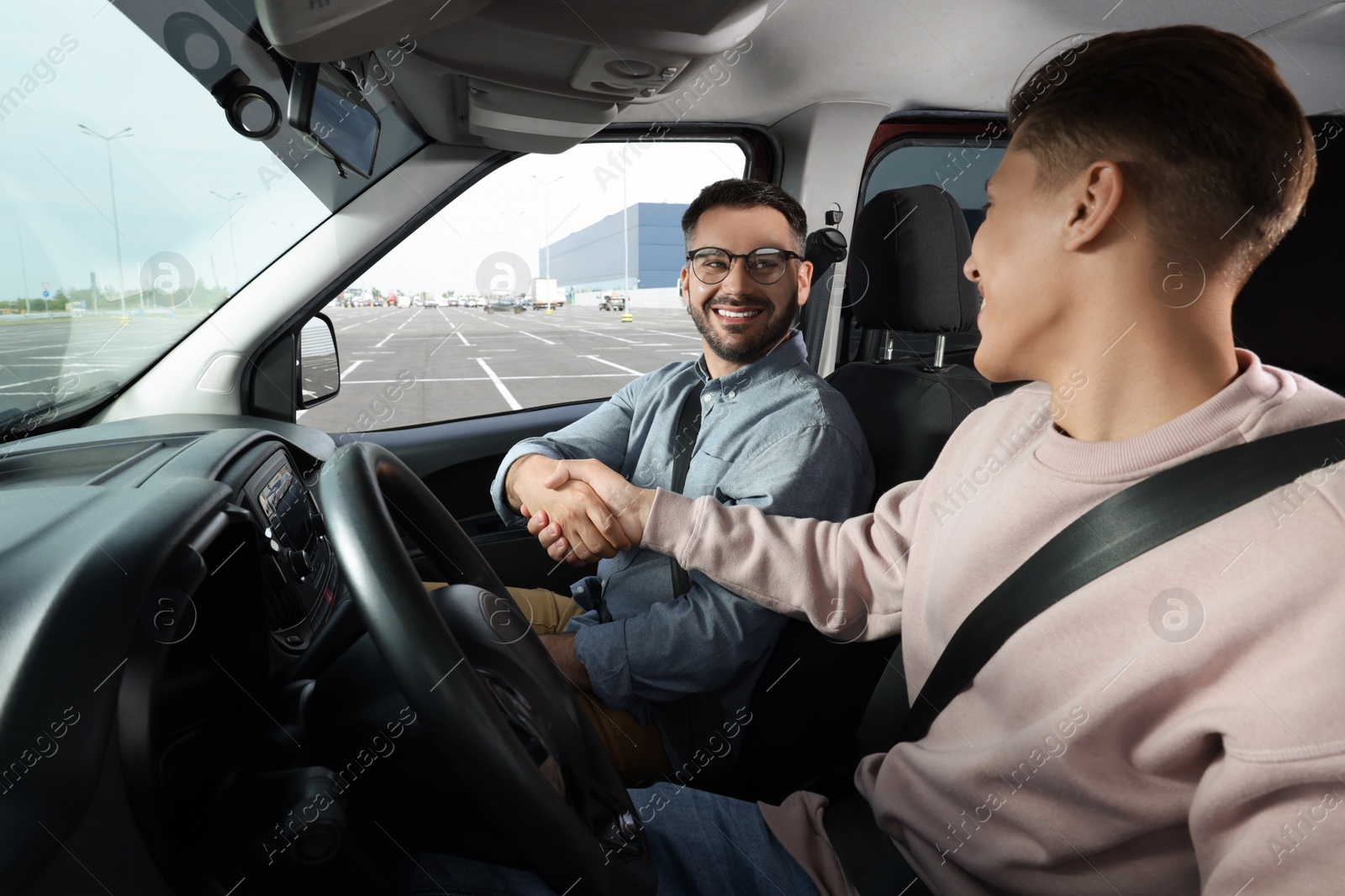 Photo of Driving school. Happy student shaking hands with driving instructor during lesson in car at parking lot