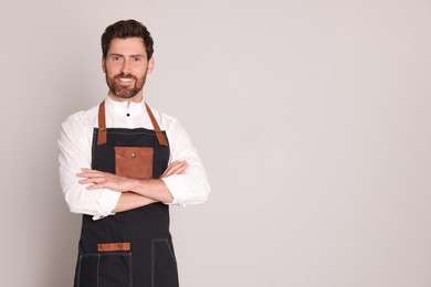 Smiling hairdresser wearing apron on light grey background, space for text