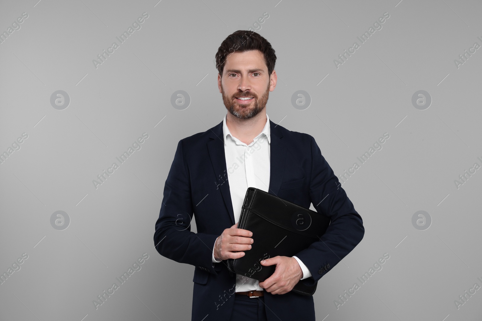 Photo of Happy real estate agent with leather portfolio on grey background