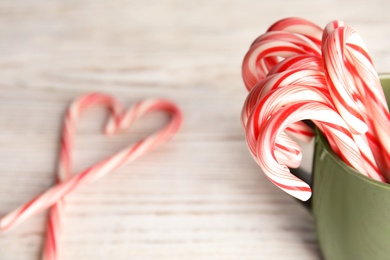 Photo of Tasty candy canes in cup on wooden table. Space for text
