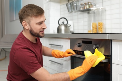 Young man cleaning oven with rag in kitchen