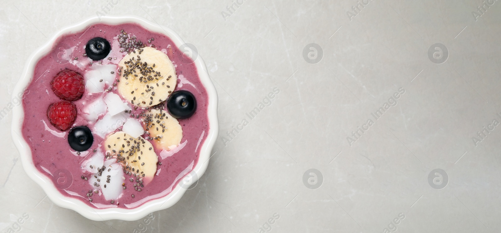 Photo of Delicious acai smoothie with fruits and coconut chips in dessert bowl on grey table, top view. Space for text