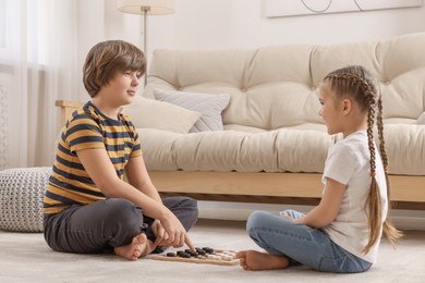 Photo of Cute boy playing checkers with little girl on floor in room