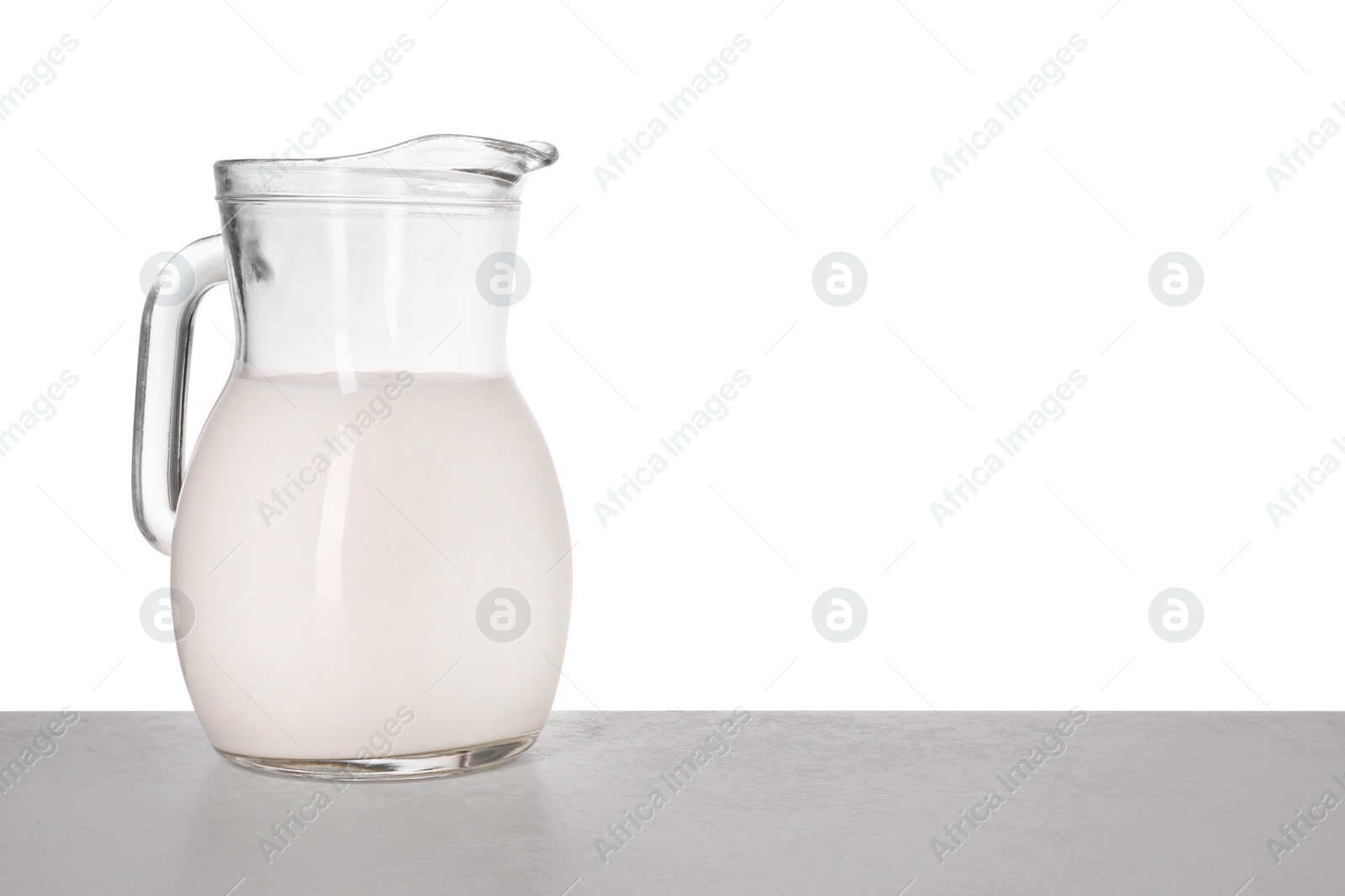 Photo of Jug of tasty milk on light table against white background