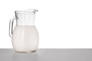 Jug of tasty milk on light table against white background