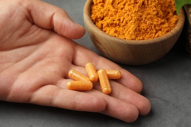 Photo of Woman with turmeric pills and aromatic powder at grey table, closeup