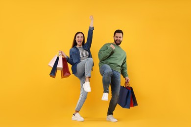 Excited couple with shopping bags having fun on orange background