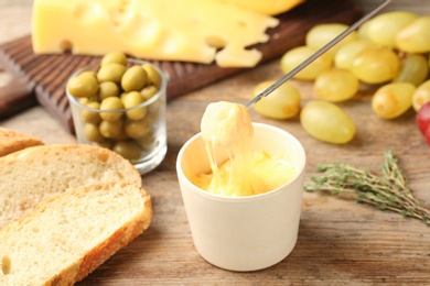 Photo of Piece of bread over bowl with delicious cheese fondue on wooden table