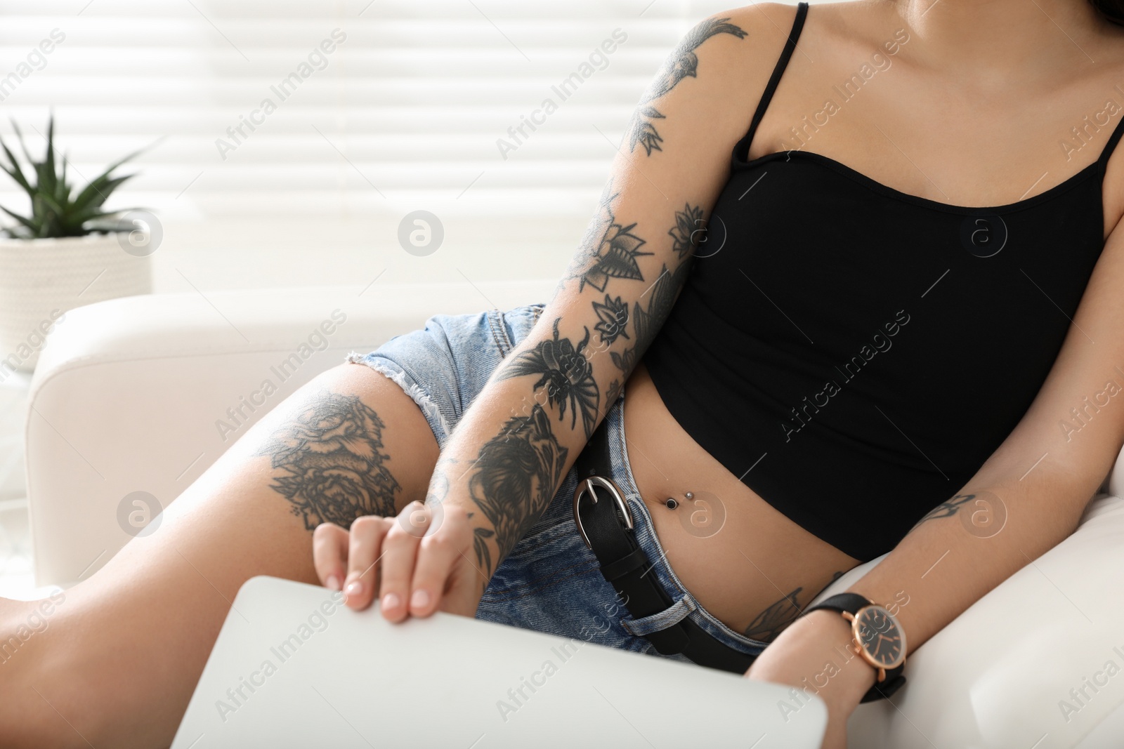 Photo of Beautiful woman with tattoos on body using laptop in living room, closeup