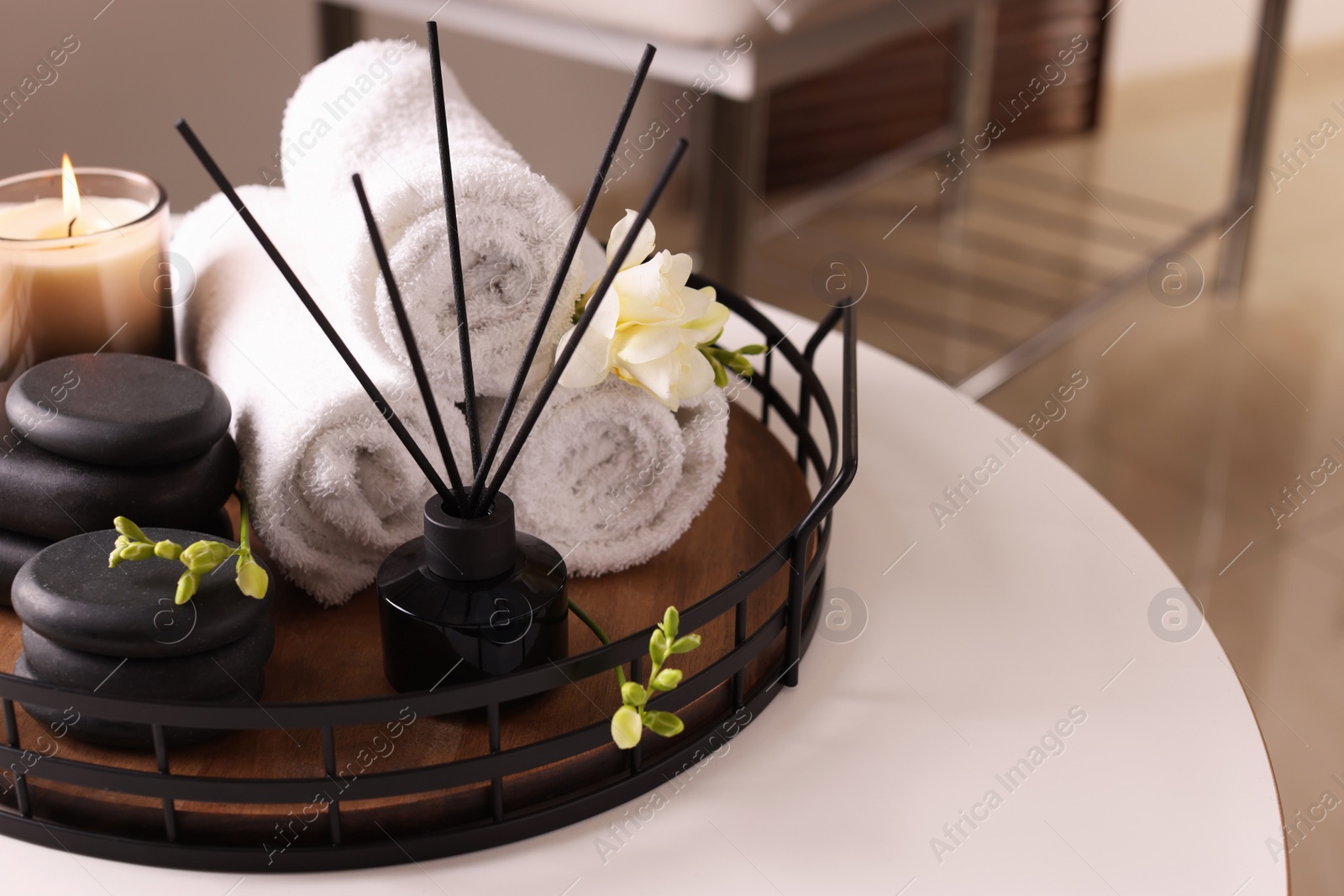 Photo of Aromatic reed air freshener, rolled towels, spa stones and candle on white table indoors