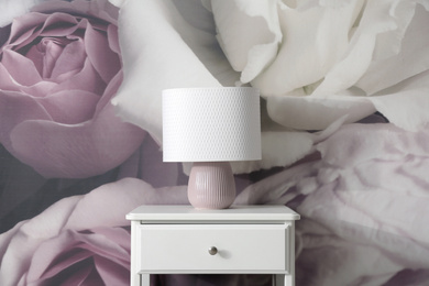 Photo of White nightstand near wall with floral wallpaper. Stylish room interior