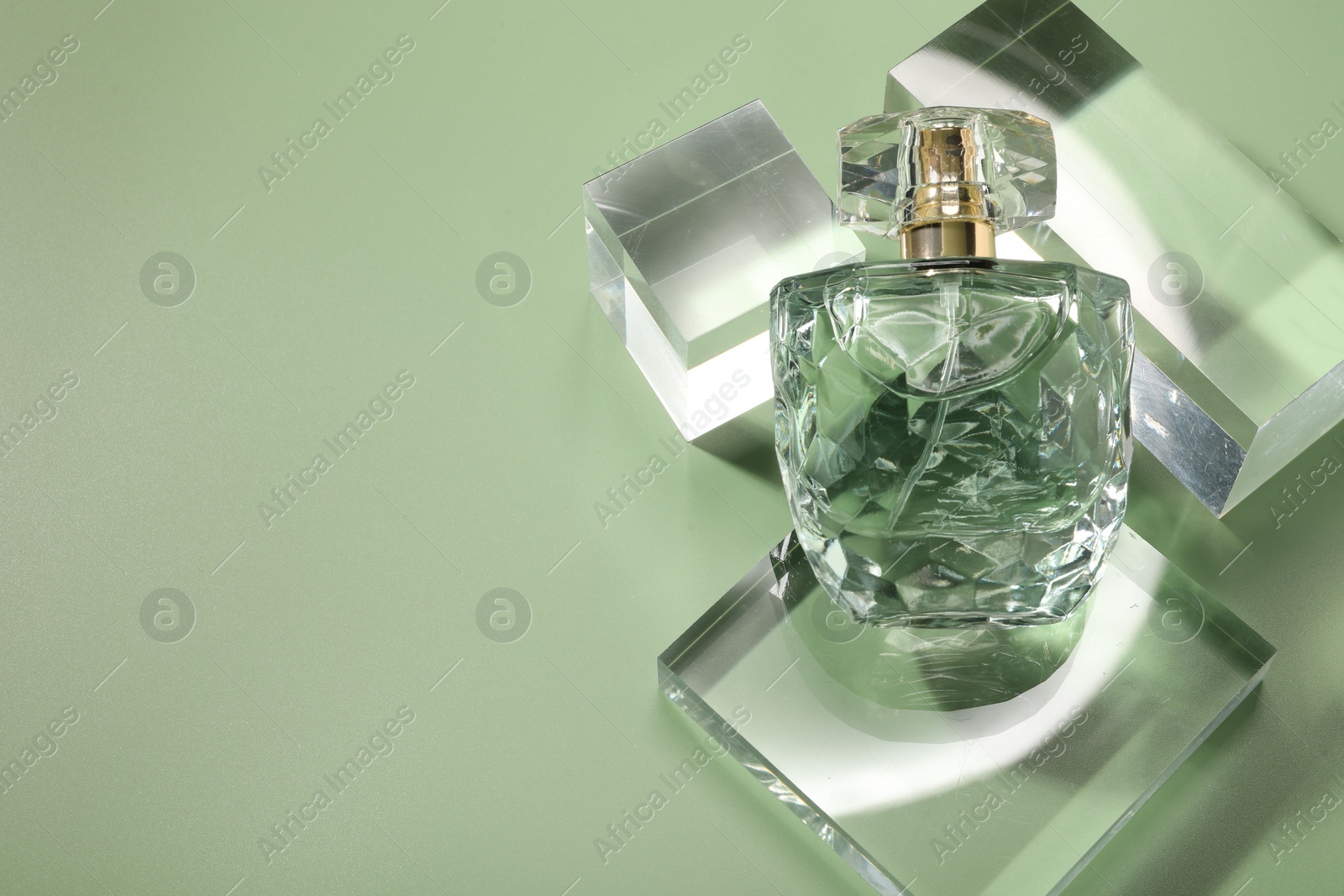 Photo of Stylish presentation of luxury perfume in sunlight on olive background, above view. Space for text