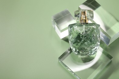 Stylish presentation of luxury perfume in sunlight on olive background, above view. Space for text