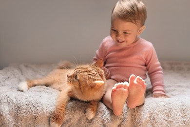 Photo of Adorable baby and cute red cat on bed indoors