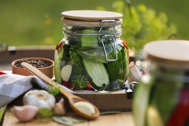 Photo of Jar of delicious pickled cucumbers and ingredients on wooden table against blurred background, closeup