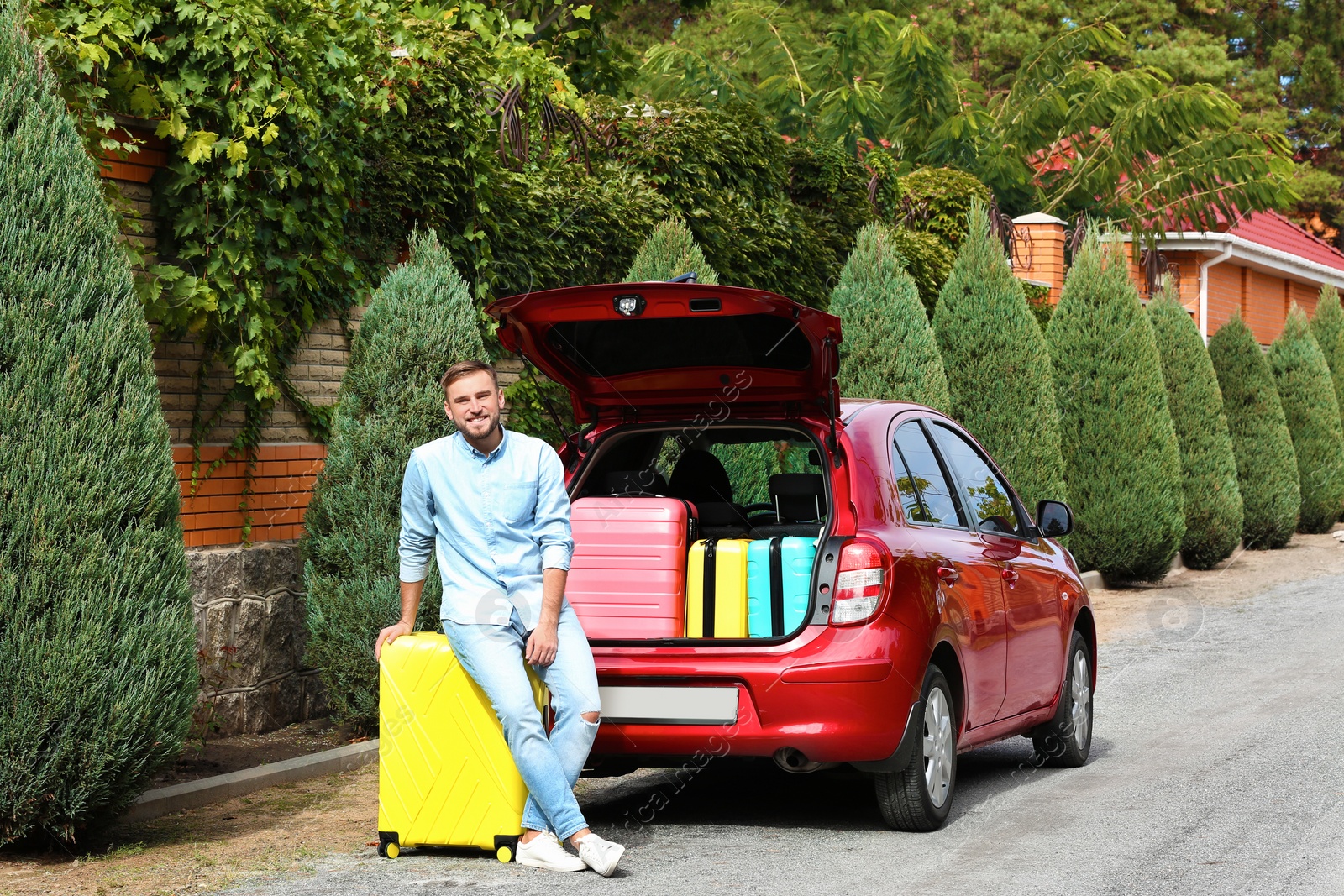 Photo of Young man standing near car trunk loaded with suitcases outdoors