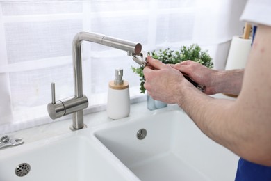 Photo of Plumber repairing faucet with spanner indoors, closeup