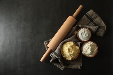 Rolling pin and different types of flour on black table, top view. Space for text