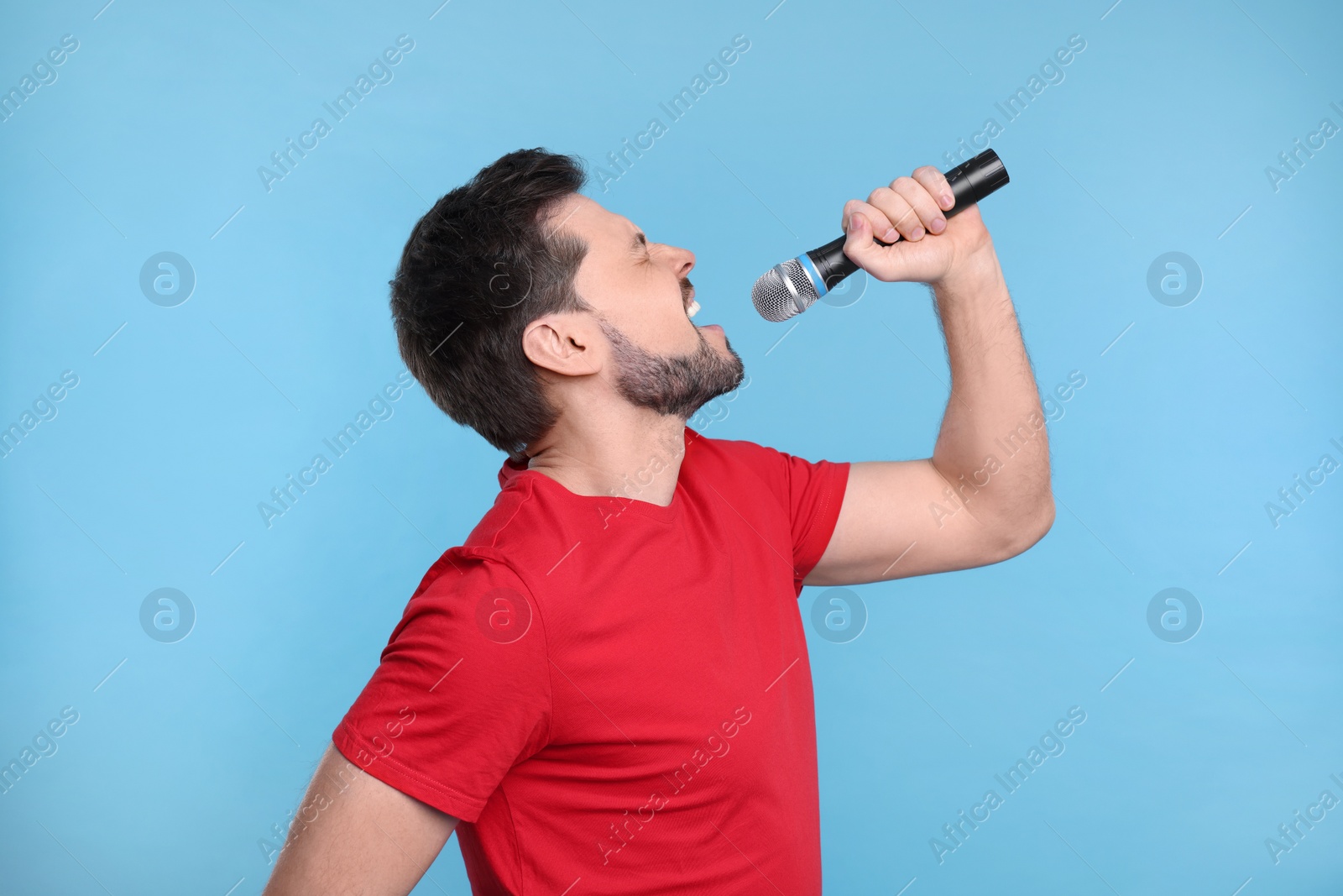 Photo of Handsome man with microphone singing on light blue background