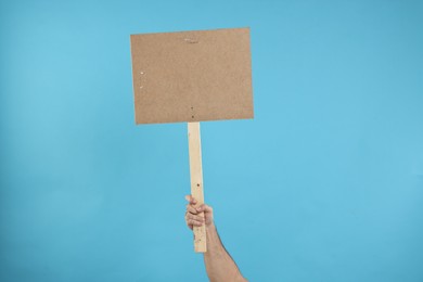 Photo of Man holding blank sign on light blue background, closeup. Space for text
