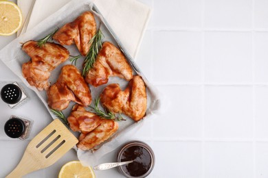 Photo of Raw chicken wings, rosemary, marinade and spices on light tiled table, flat lay. Space for text
