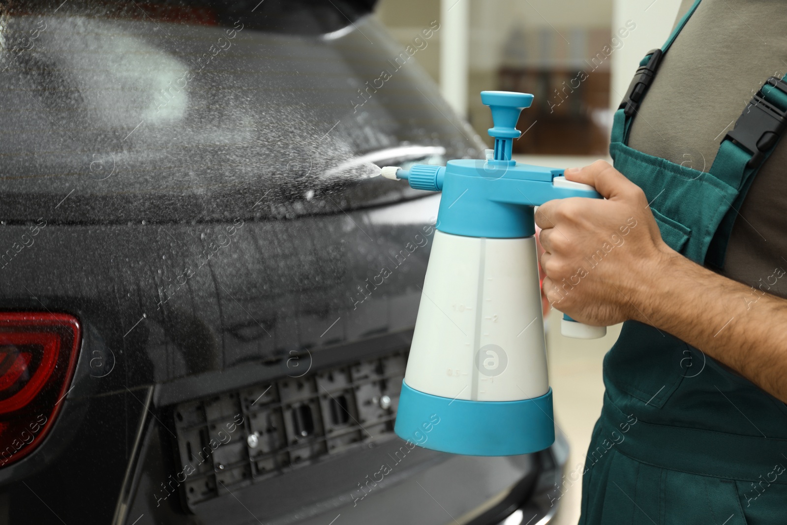 Photo of Worker spraying water onto car window before tinting in workshop, closeup