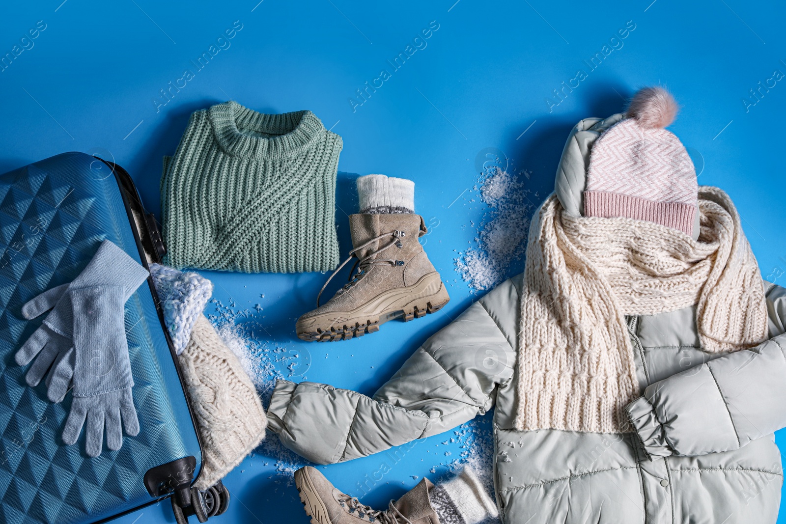 Photo of Suitcase with warm clothes on light blue background, flat lay. Winter vacation