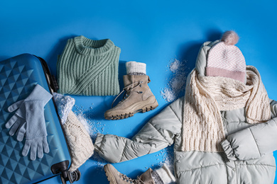 Photo of Suitcase with warm clothes on light blue background, flat lay. Winter vacation
