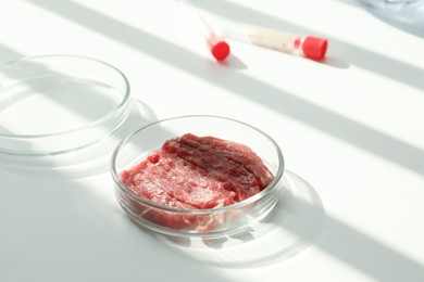 Petri dish with pieces of raw cultured meat on white table in laboratory, space for text