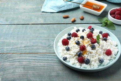 Photo of Delicious cottage cheese with fresh berries and honey served on light blue wooden table, space for text. Tasty breakfast