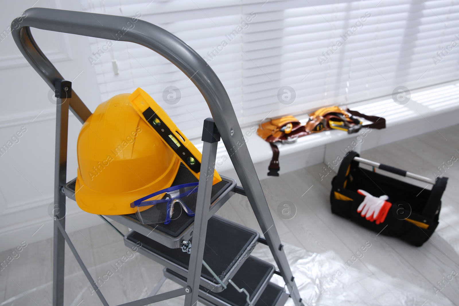 Photo of Metal stepladder with hardhat, level and protective goggles indoors, above view