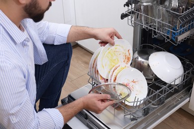 Man loading dishwasher with dirty plates indoors, closeup
