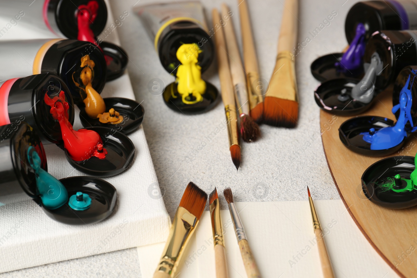 Photo of Tubes of colorful paints and brushes on textured table