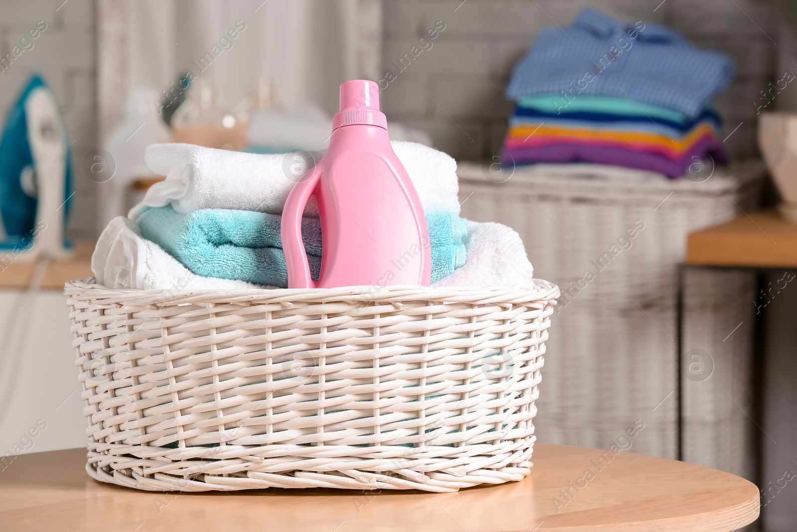 Photo of Laundry basket with clean towels and bottle of detergent on table