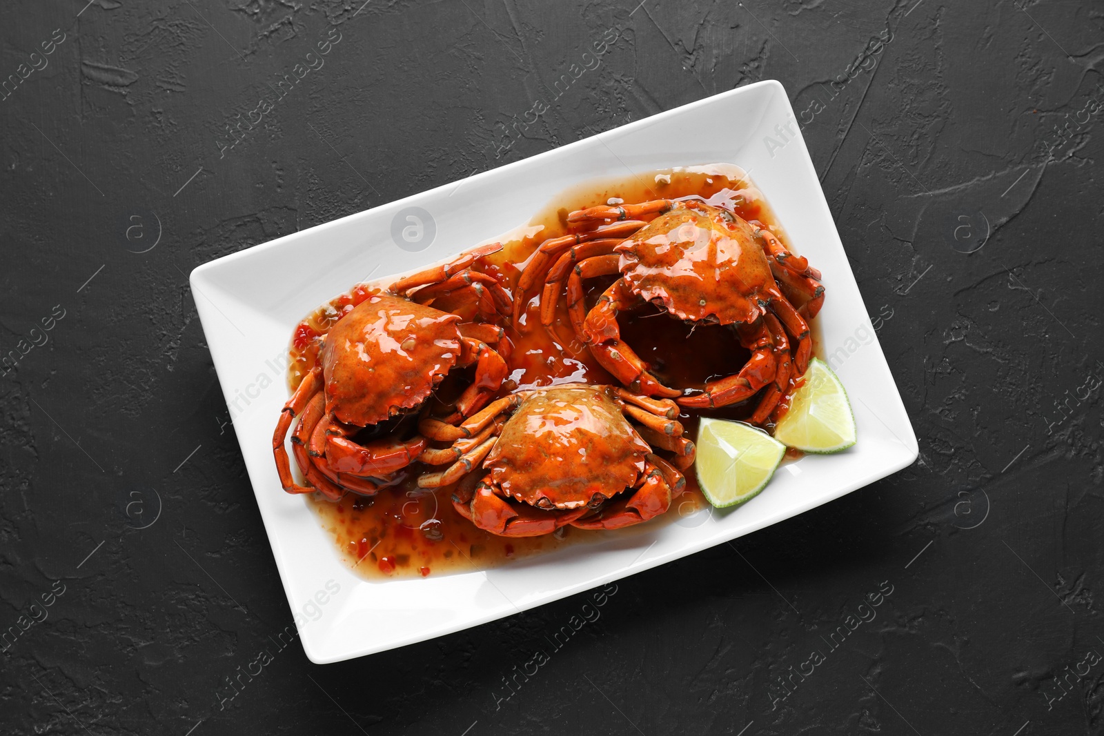 Photo of Delicious boiled crabs with sauce and lime on black textured table, top view