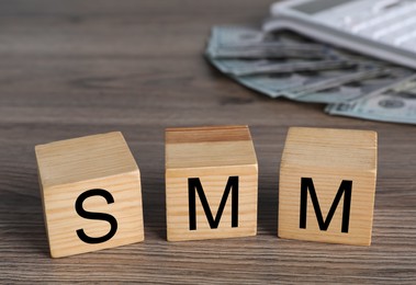 Photo of Cubes with abbreviation SMM (Social media marketing), money and calculator on wooden table