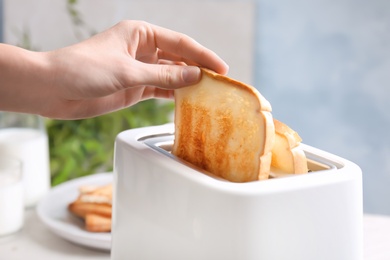 Woman taking slice of bread from toaster, closeup