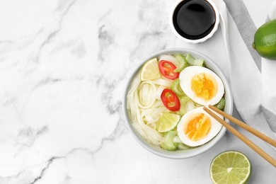 Photo of Bowl of delicious rice noodle soup with celery and egg on white marble table, flat lay. Space for text