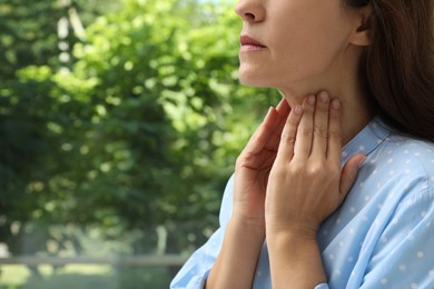Photo of Mature woman doing thyroid self examination near window, closeup. Space for text