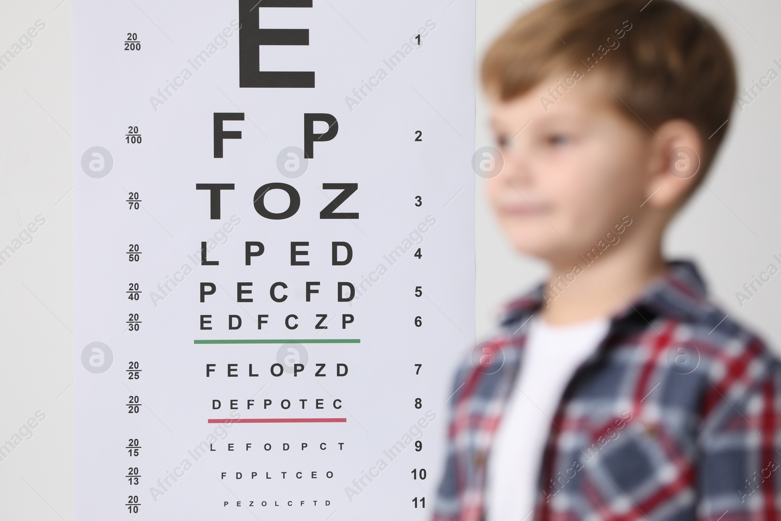 Photo of Cute little boy against vision test chart, selective focus