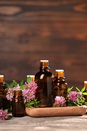 Bottles with essential oils, clover and rosemary on wooden table. Space for text