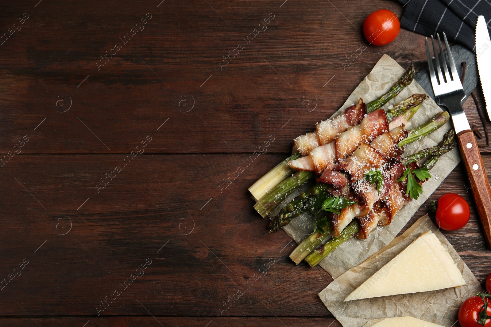 Photo of Oven baked asparagus wrapped with bacon on wooden table, flat lay. Space for text