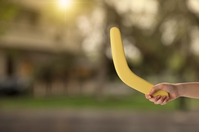 Woman holding yellow boomerang outdoors, closeup. Space for text