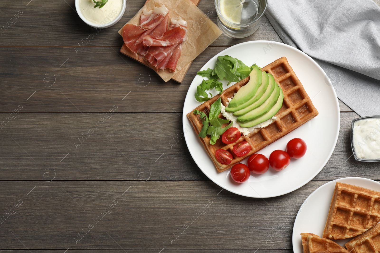 Photo of Fresh Belgian waffles with avocado, tomatoes and arugula on wooden table, flat lay. Space for text