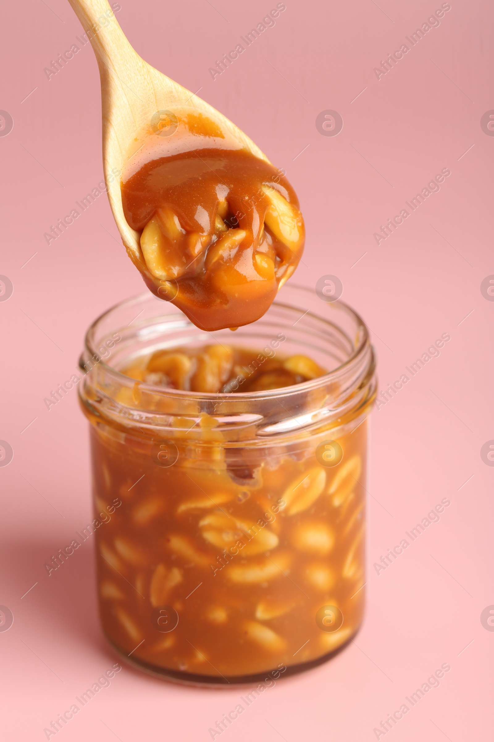 Photo of Taking tasty salted caramel with peanuts from jar on pink background, closeup