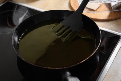 Photo of Frying pan with used cooking oil and spatula on stove, closeup