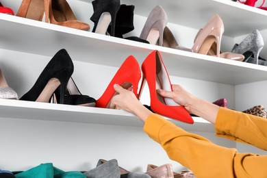 Photo of Woman taking high-heeled shoes from shelving unit, closeup